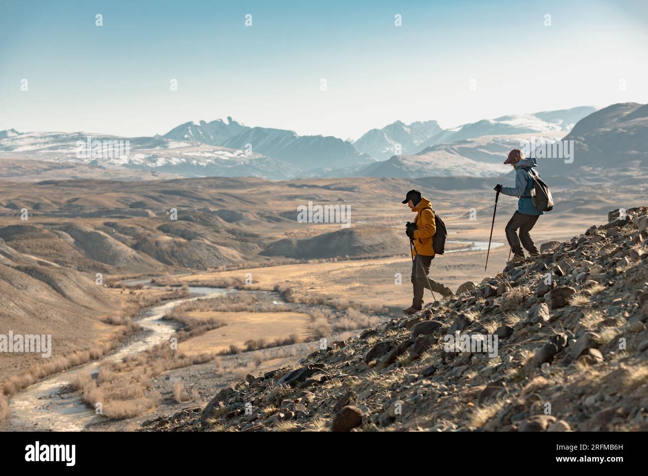 Zwei junge Wanderer mit Rucksäcken und Wanderstöcken wandern bergab in den Bergen. Aktiver Tourismus in den Bergen Stockfoto
