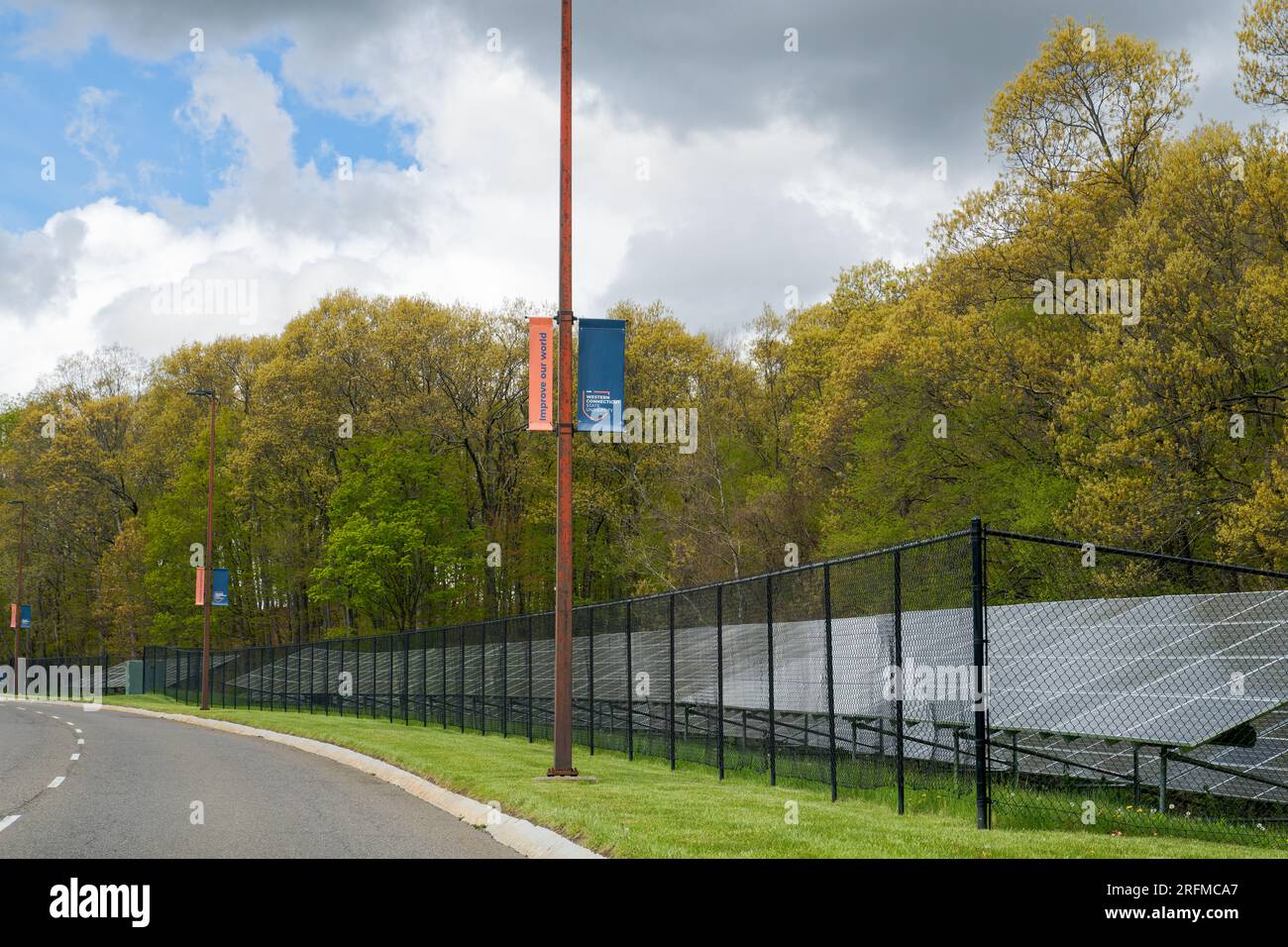 Danbury, CT - 3. Mai 2023: Banner der Western Connecticut State University mit „Improve our World“ entlang des University Boulevard mit einem Solarpaneel b Stockfoto