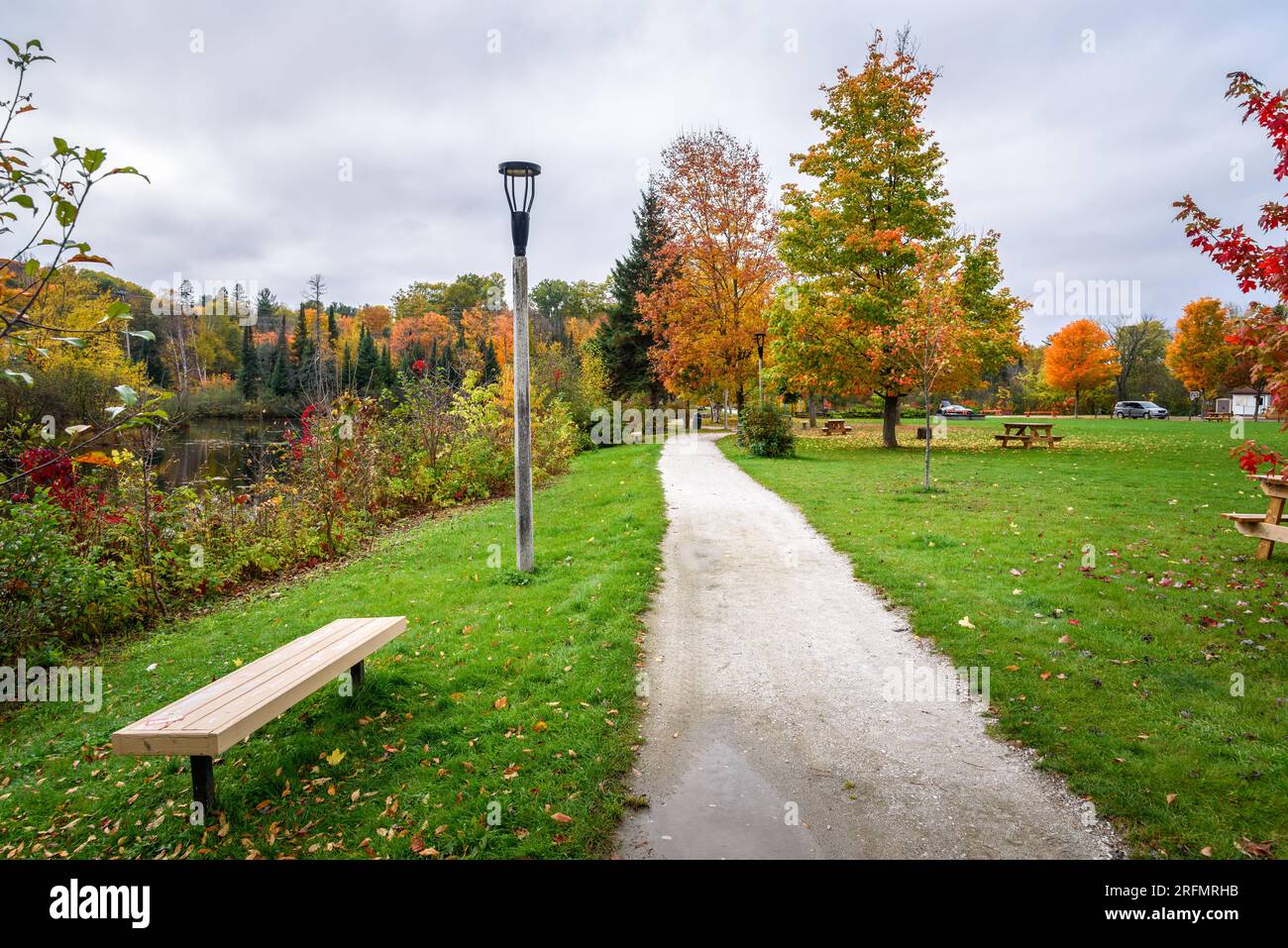 Verlassener Wanderweg, gesäumt von Laternenpfosten und Bänken in einem Flusspark an einem bedeckten Herbsttag Stockfoto