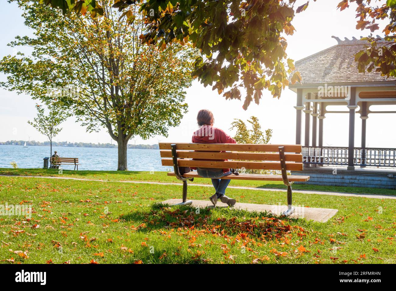 Eine Frau, die sich entspannt und einen warmen Herbstmorgen genießt, während sie auf einer Bank im Park am See sitzt Stockfoto