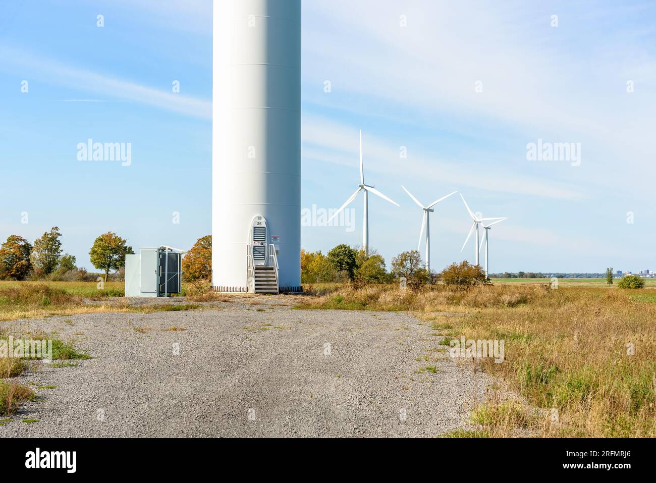 Tür an der Basis eines Turms, der an einem sonnigen Herbsttag eine Windturbine auf dem Land unterstützt. Andere Windturbinen sind im Hintergrund sichtbar. Stockfoto