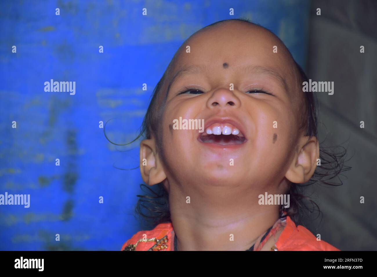 Süßes kleines Mädchen, das ein Smiley-Gesicht macht, mit blauem Hintergrund Stockfoto