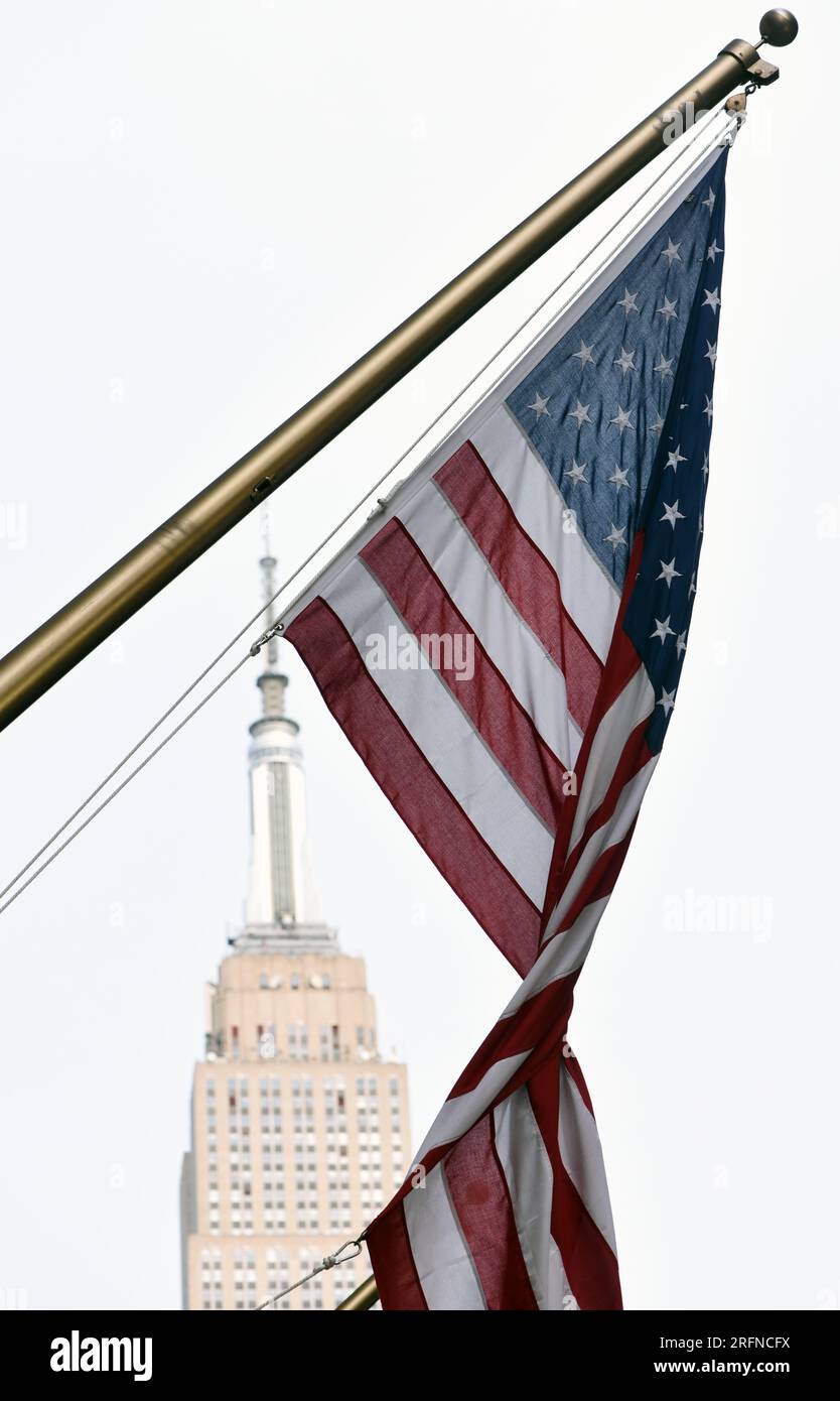 Vor dem Empire State Building in New York City hängt eine verdrehte amerikanische Flagge mit Sternen und Streifen. Stockfoto