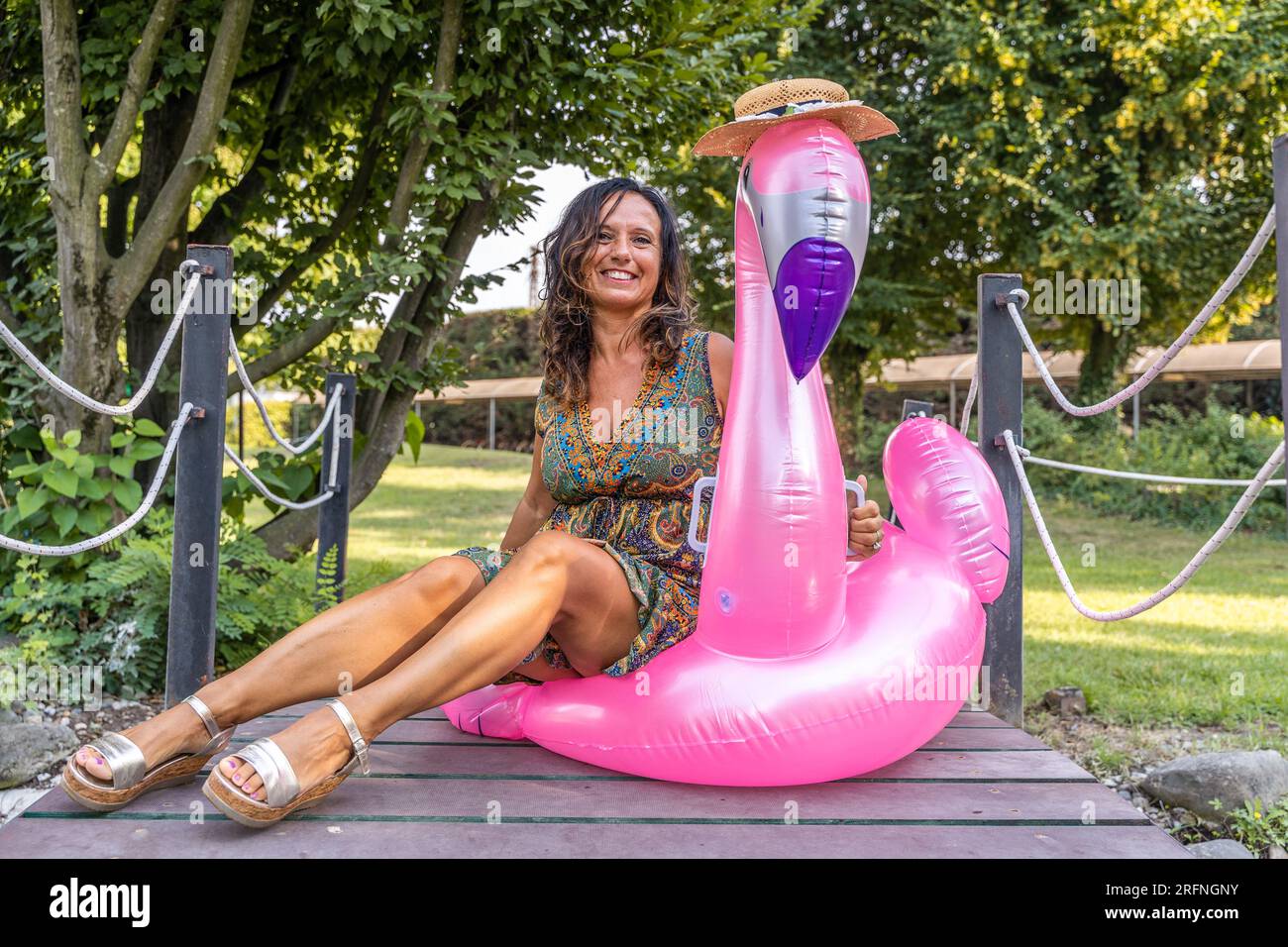 Porträt einer schönen Frau mittleren Alters, die auf einem aufblasbaren, pinkfarbenen Flamingo-Spielzeug sitzt Stockfoto
