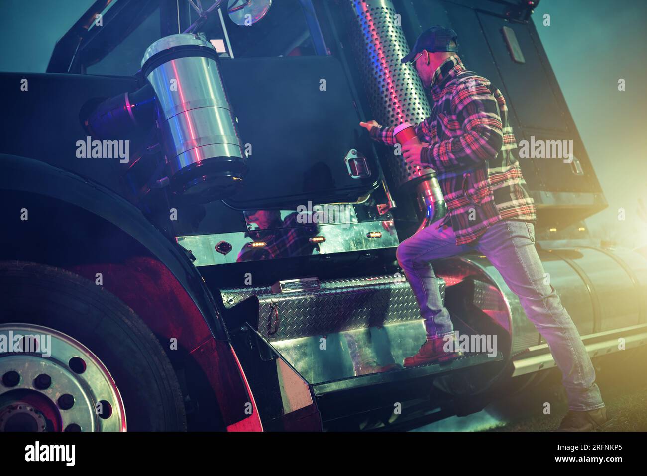 American Semi Truck Driver mit einer Tasse heißem Kaffee in der Hand verlässt Truck Stop bei Nacht. Stockfoto