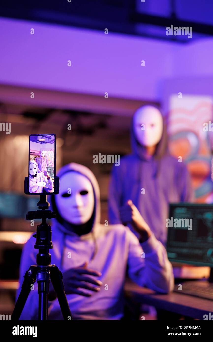Smartphone-Bildschirm mit Hackern, die ein Bedrohungsvideo aufnehmen und das Opfer nach vertraulichen Informationen und Geld fragen. Kriminelle tragen anonyme Masken, die nachts Online- und Streaming-Betrug drohen Stockfoto