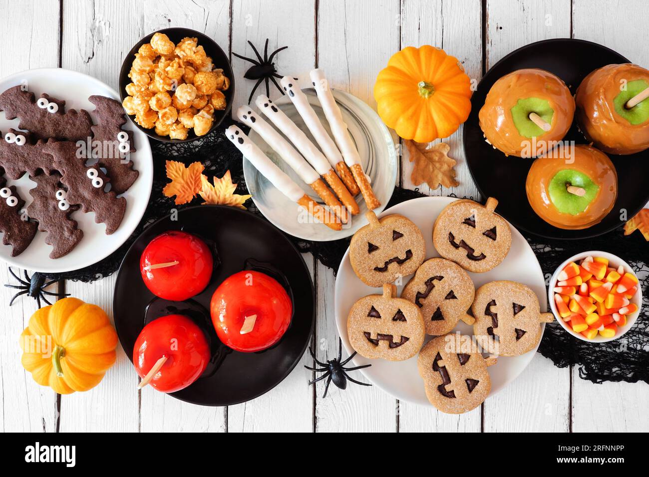 Traditionelle Halloween-Tischszene mit weißem Holzhintergrund. Draufsicht. Eine Gruppe kandierter Äpfel, Kekse, Süßigkeiten und Süßigkeiten. Stockfoto