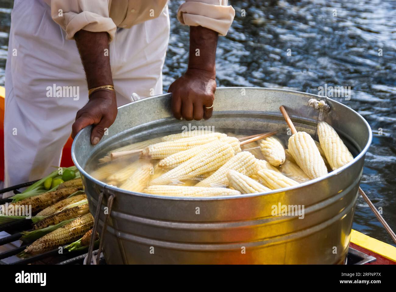 Nahaufnahme der Hände eines Straßenverkäufers, der eine große, mit gekochtem Mais gefüllte Wanne sicher hält, ein beliebter Snack in Xochimilco, Mexiko. Stockfoto