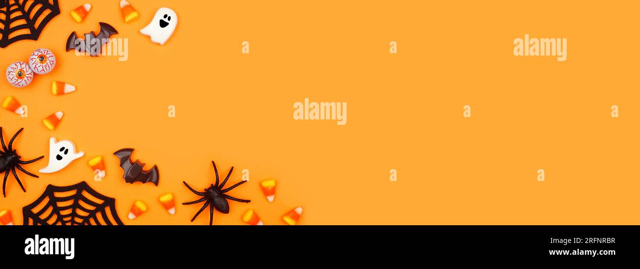 Halloween-Eckrahmen mit verstreuten Süßigkeiten und Dekor. Über der Ansicht über einem orangefarbenen Bannerhintergrund mit Kopierbereich. Stockfoto