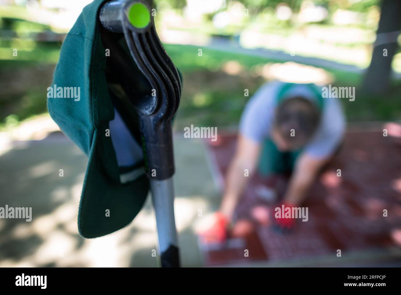 Eine grüne Baseballkappe hängt am Griff einer Schaufel, und im Hintergrund legt ein Arbeiter Pflastersteine. Stockfoto