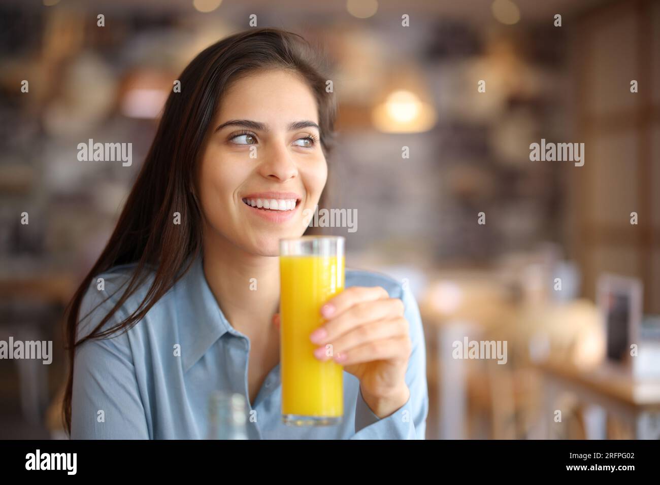 Eine glückliche Frau, die Orangensaft trinkt, sieht in einer Bar im Inneren weg Stockfoto