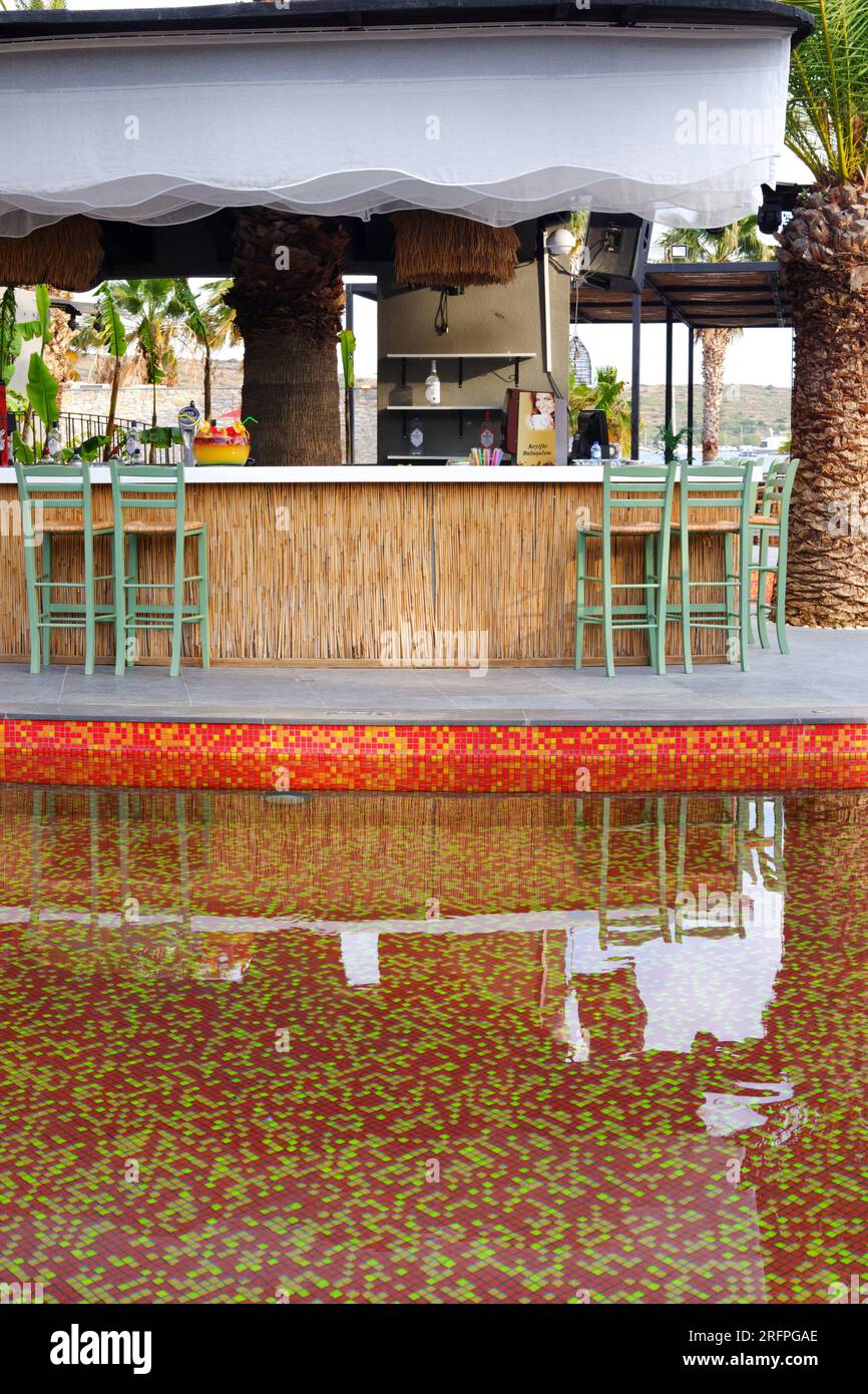 Tropic Bar am Pool an einem Sommertag mit Palmen im Hintergrund. Reflexion über Wasser und Stühle. Stockfoto