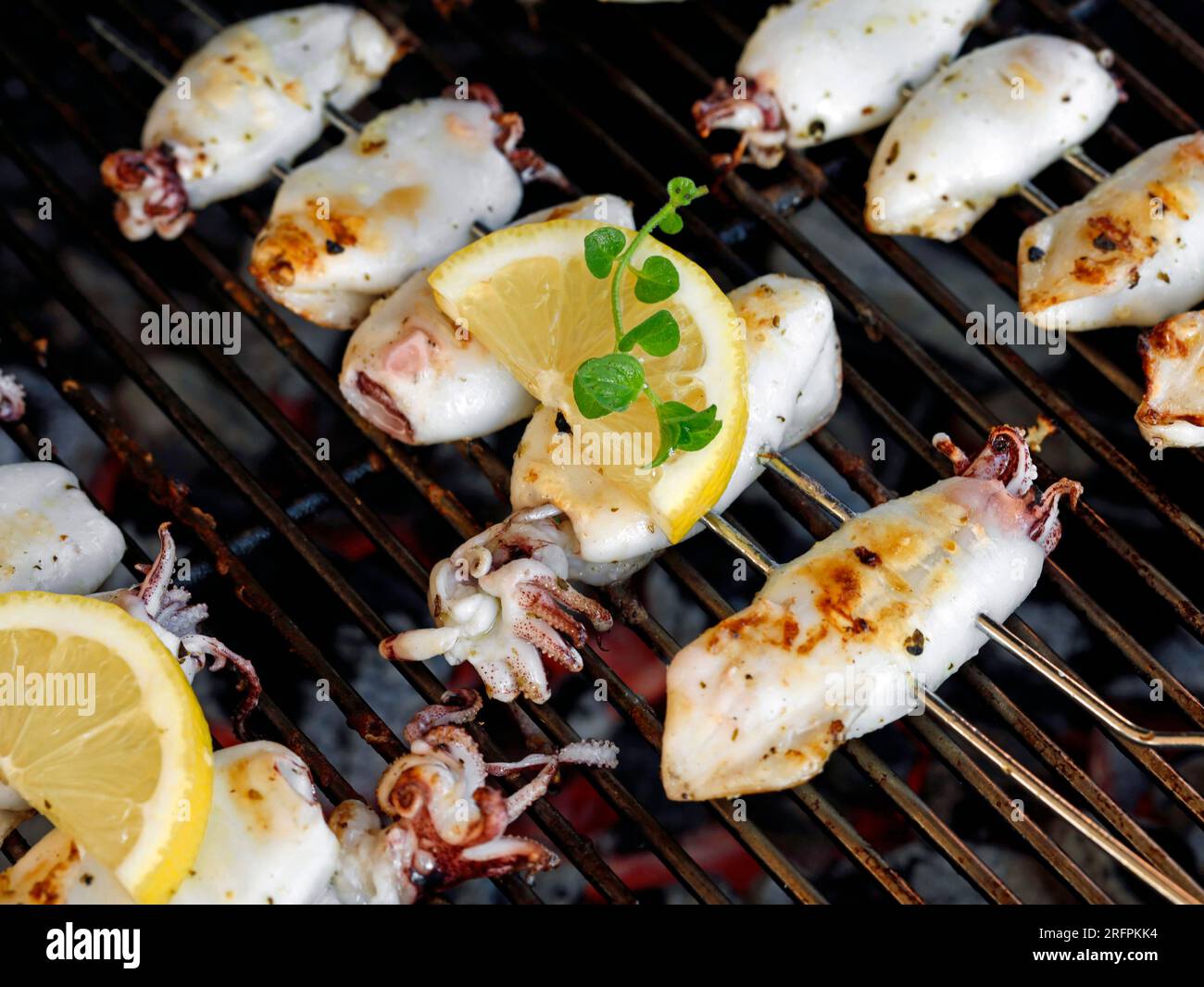 Nahaufnahme von frisch gegrillten Tintenfischspießen auf Holzkohlegrill mit Zitrone und frischem Oregano, köstliche gegrillte Meeresfrüchte Stockfoto
