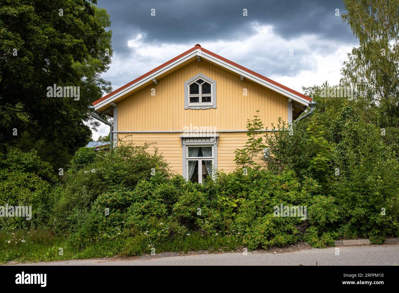 Altes gelbes Holzhaus, umgeben von Büschen an einem bewölkten Tag im Mathilldedal Village - Tagesausflug Ziel, Perniö, Finnland Stockfoto