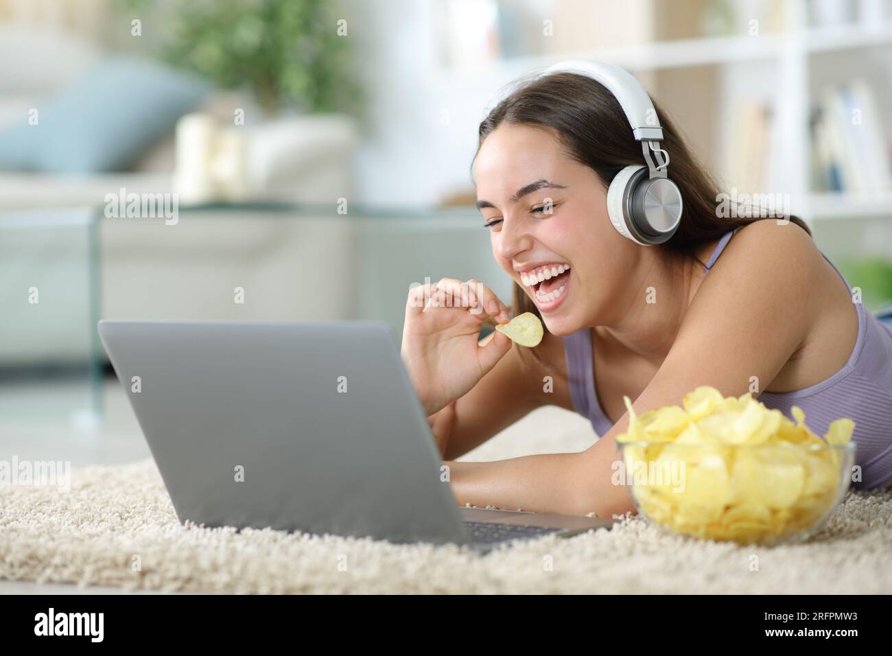 Lustige Frau, die Chips isst und sich zu Hause Online-Videos in einem Laptop ansieht Stockfoto