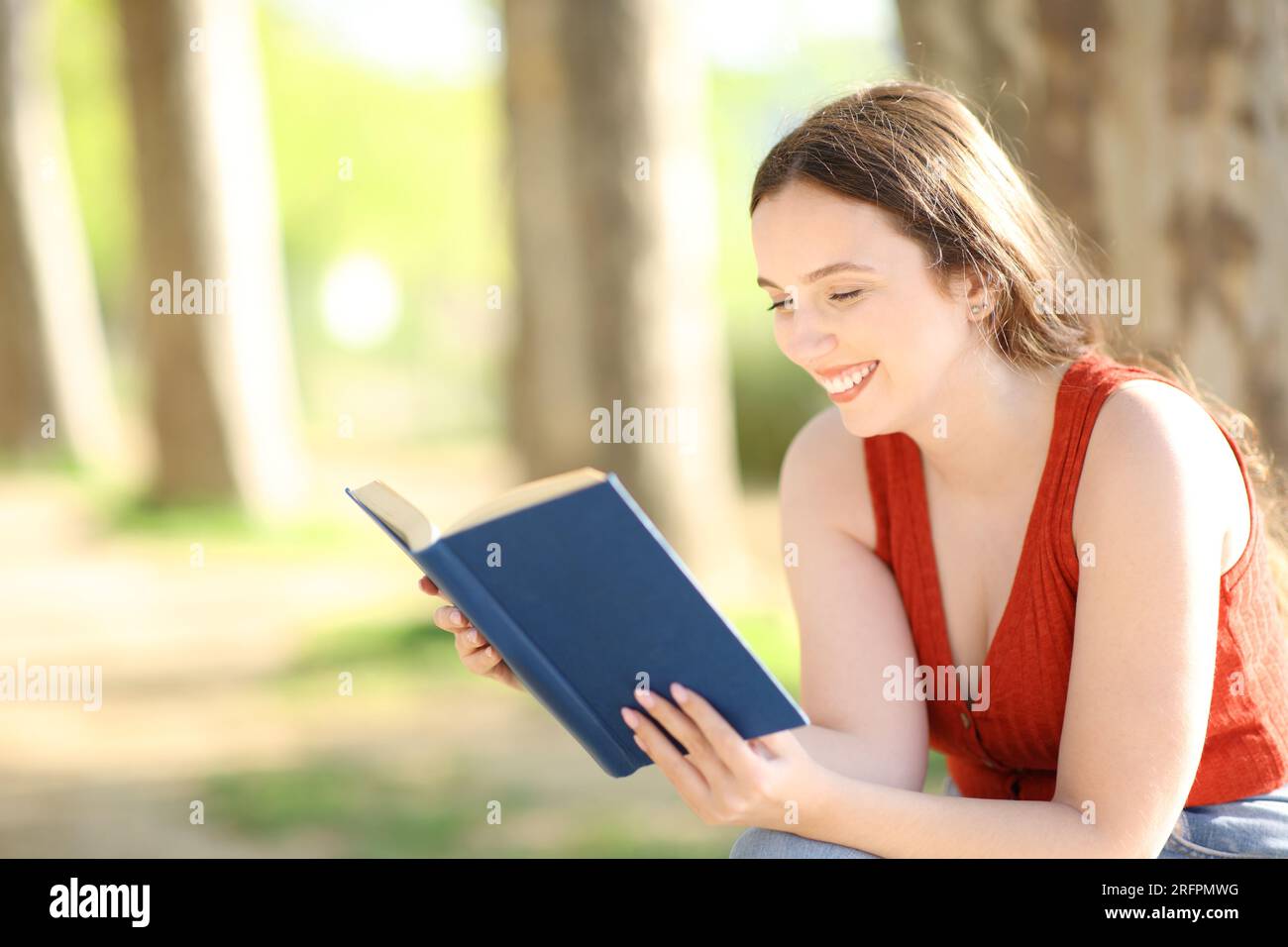 Eine glückliche Frau, die ein Papierbuch liest und im Park sitzt Stockfoto