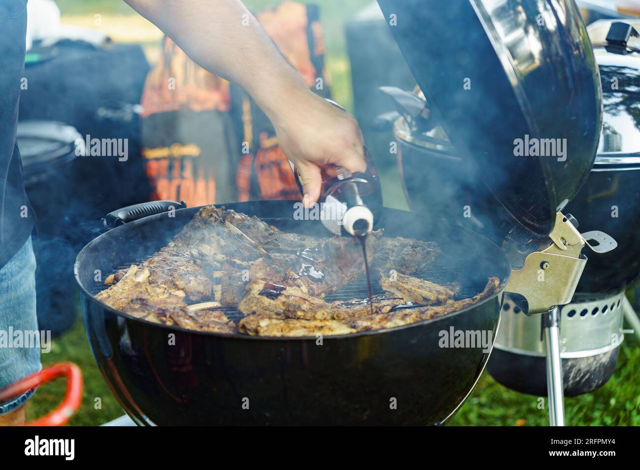 Ein Mann kocht im Sommer Schweinerippchen auf dem Grill im Hof und gießt Soße darüber Stockfoto