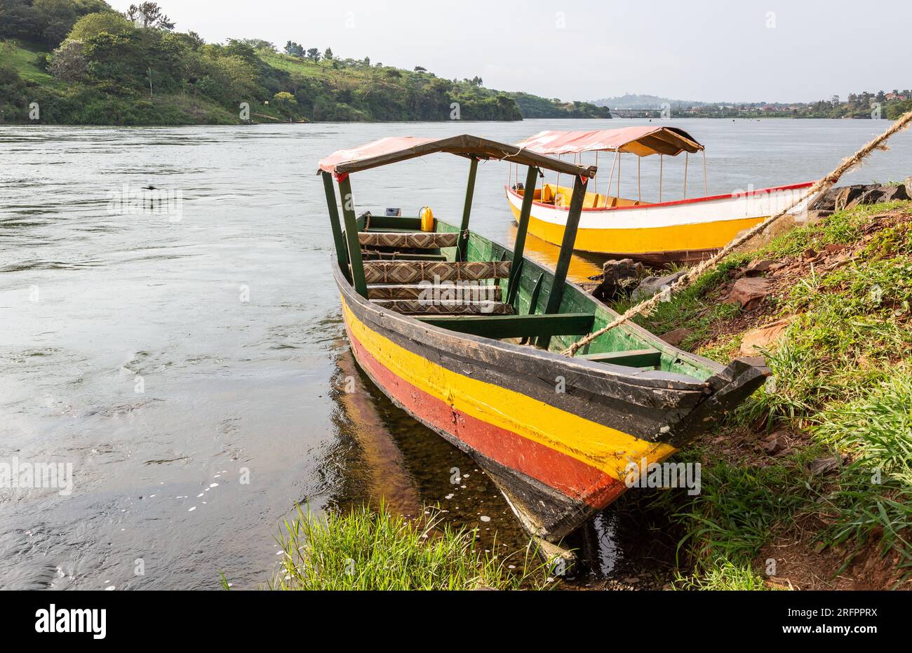 Zwei Holzboote, in hellen Farben bemalt, erwarten Touristen für einen Ausflug auf dem aufsteigenden Nil. Jinja, Uganda. Stockfoto