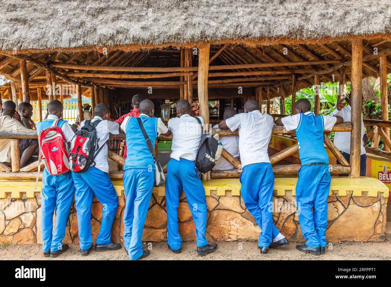 Sechs Männer in blauen Hosen lehnen sich am Eingang einer Bar. Jinja, Uganda. Stockfoto