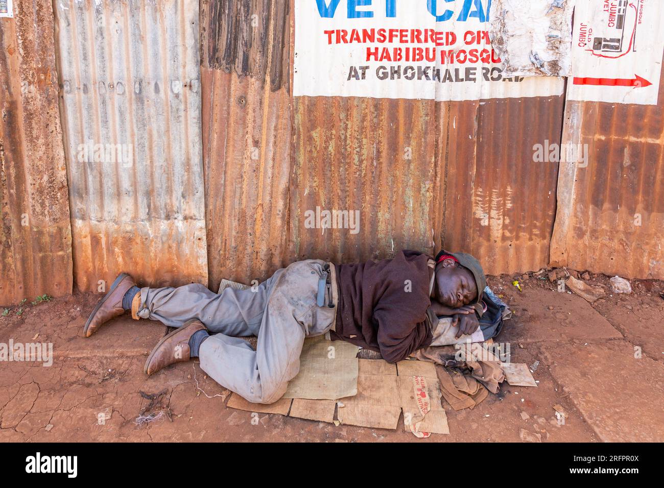 Ein Mann, der ein Nickerchen macht und auf Pappe auf der Straße liegt. Jinja, Uganda. Stockfoto