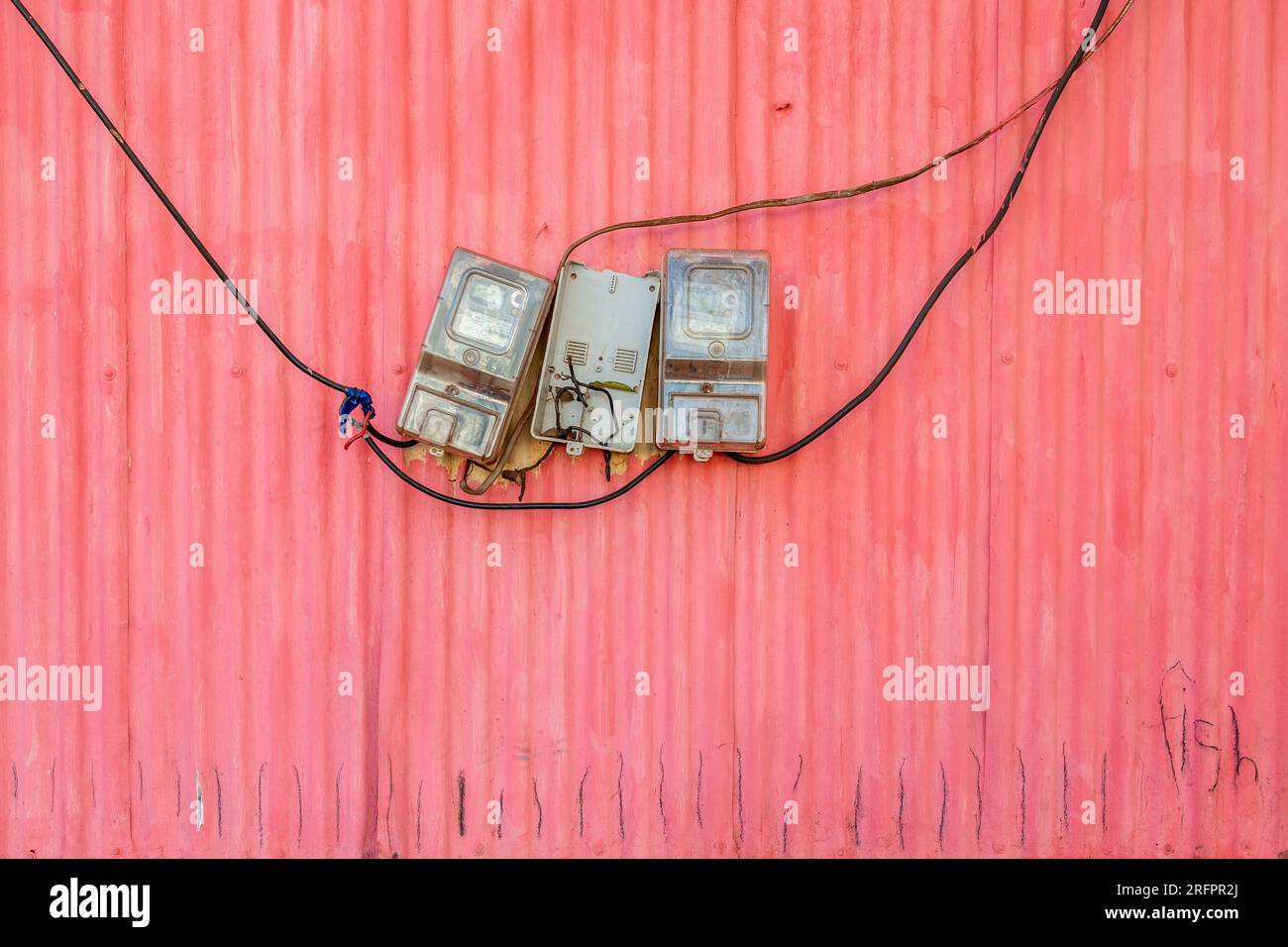 Elektrische Zähler hangen achtlos an einer rosa Blechwand. Jinja, Uganda. Stockfoto