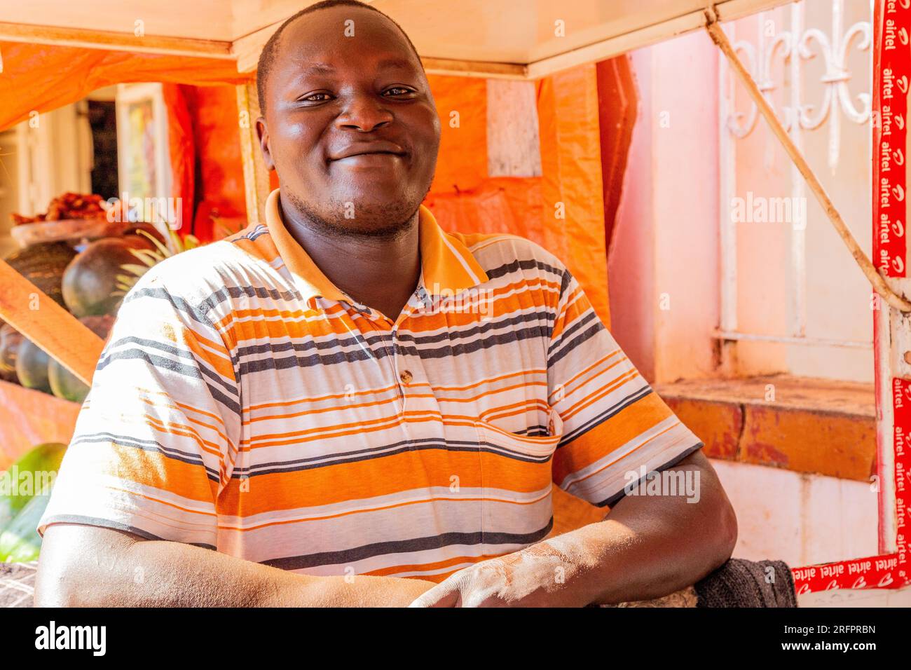 Porträt eines lächelnden Mannes in oranger Umgebung. Jinja, Uganda. Stockfoto
