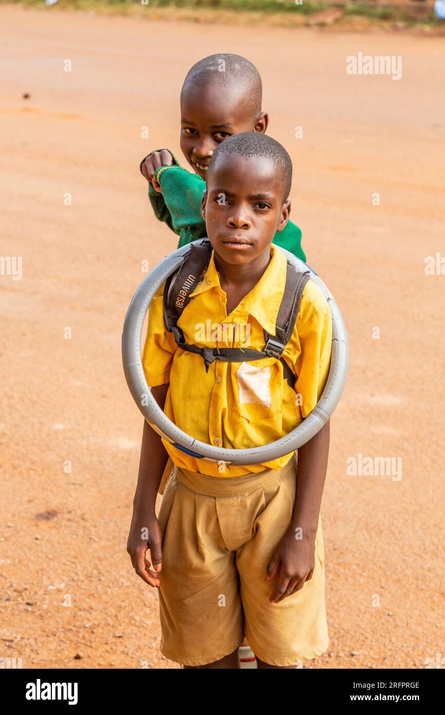 Zwei Kinder posieren, eines trägt eine Lenkradabdeckung um den Hals. Jinja, Uganda. Stockfoto