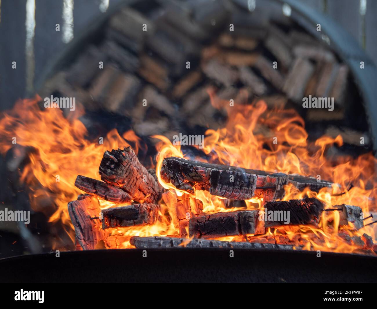 Holz brennt auf einer Feuerstelle mit einem Holzhaufen im Hintergrund Stockfoto