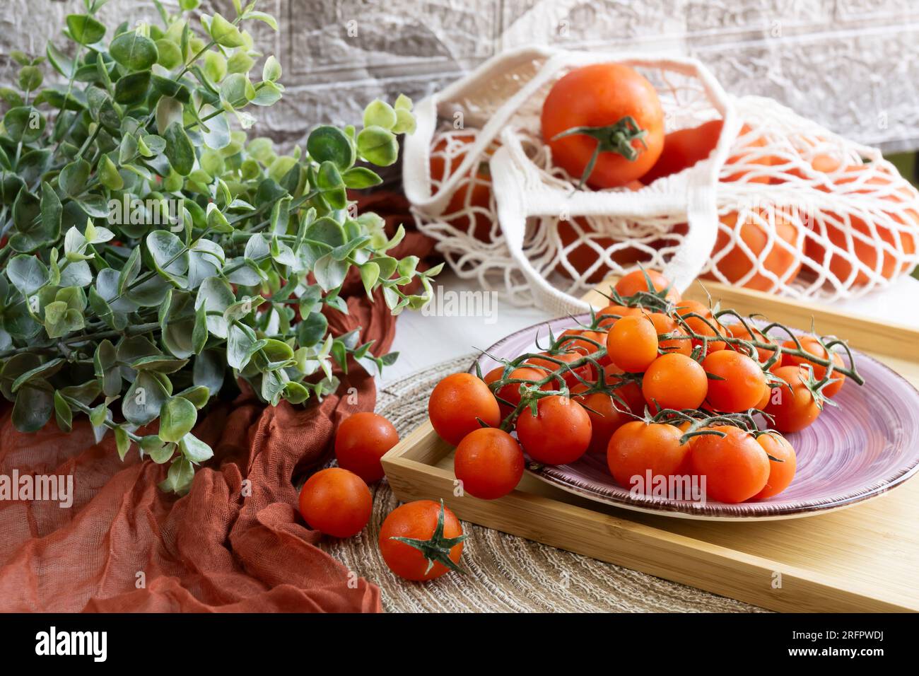 Rote Tomaten in einer nachhaltigen Einkaufstasche und Kirschtomaten in einem Holztablett mit einigen grünen Blättern. Stockfoto