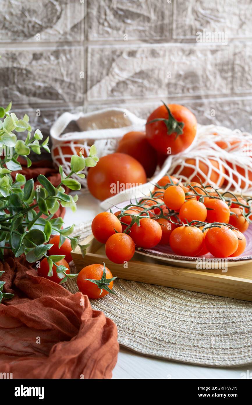 Rote Tomaten in einer nachhaltigen Einkaufstasche und Kirschtomaten in einem Holztablett mit einigen grünen Blättern. Stockfoto