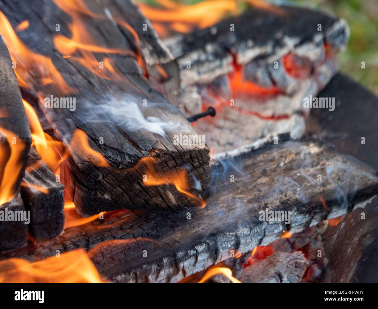 Feuerholz, das auf ein Feuer strahlt, orangefarbene Flammen, Rauch, heiße Glut Stockfoto