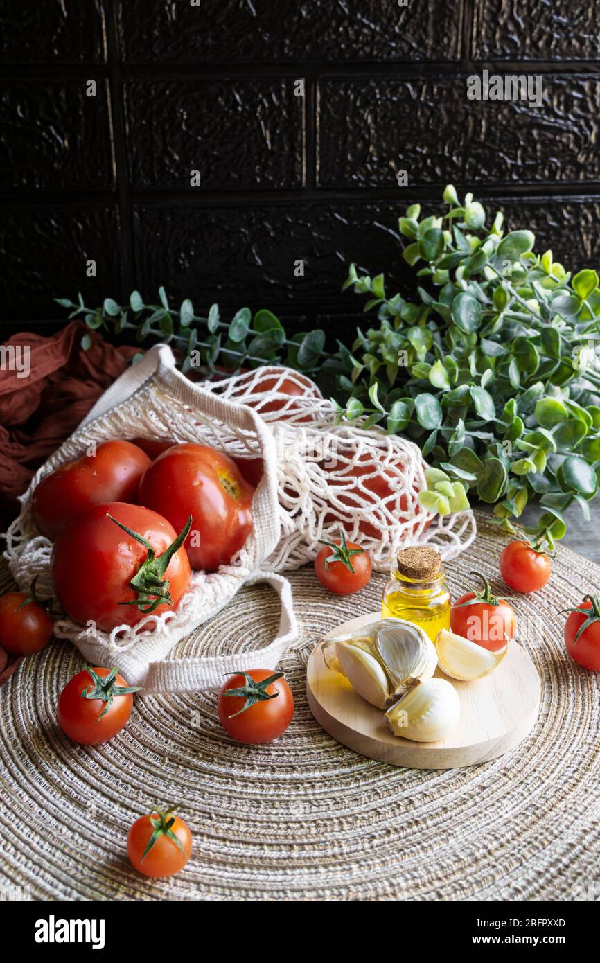 Vertikaler Schuss roter Tomaten in einer ökologischen Einkaufstasche mit Olivenöl und Knoblauch an der Seite. Stockfoto
