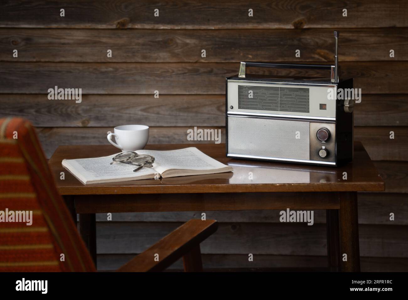 Vintage-Radioempfänger auf einem alten Tisch mit altmodischer Brille, Buch und Sessel Stockfoto