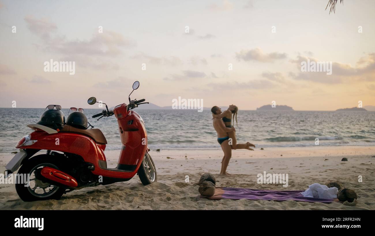 Motorroller Road Trip. Schönes Paar auf rotem Motorrad in weißen Kleidern am Sandstrand. Hochzeit gerade verheiratete Menschen, die in der Nähe von tropischen Palmen, Meer. Flitterwochen am Meer. Asien Thailand. Motorradmiete. Stockfoto