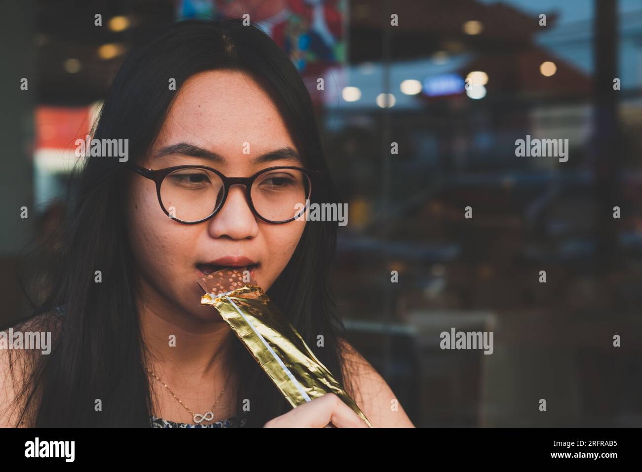 Eine junge, glückliche Frau, die Schokoriegel beißt. Das Lifestyle-Food-Konzept der Menschen Stockfoto