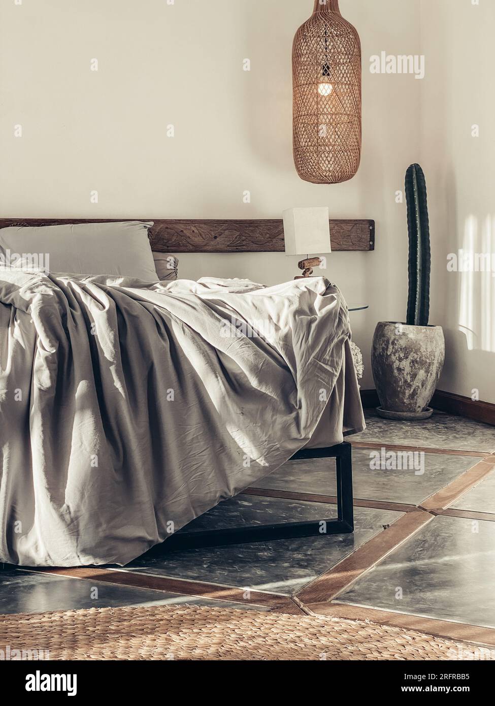 Schlafzimmer im Loft-Stil mit grauer Bettwäsche, Korblampe zum Aufhängen und Nachttisch Stockfoto