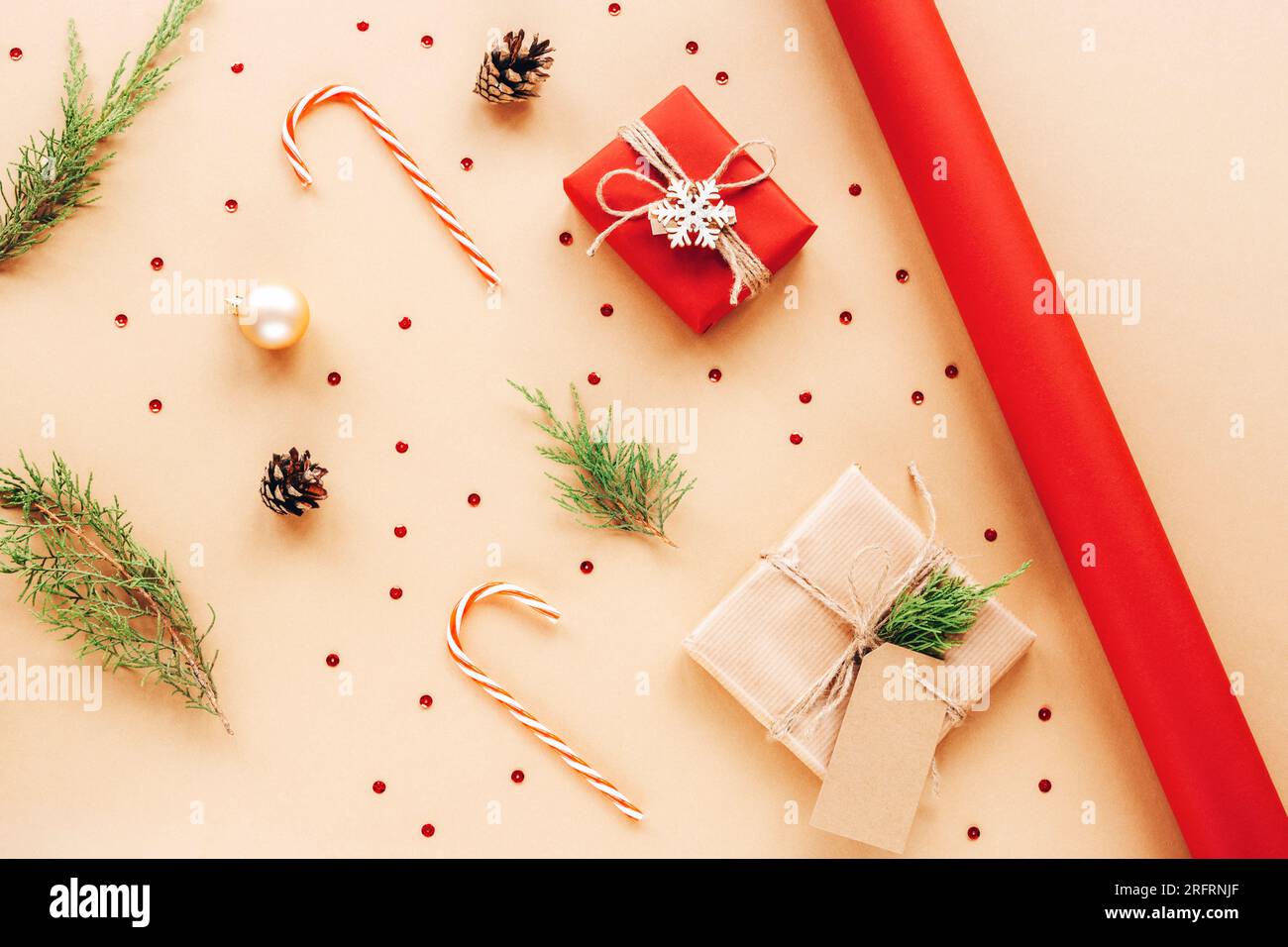 Geschenkschachteln, Zuckerstangen und Zypressenäste. Weihnachtszubereitung von Geschenken mit rotem und beigefarbenem Geschenkpapier. Neujahrskonzept. Draufsicht, flach liegend. Stockfoto