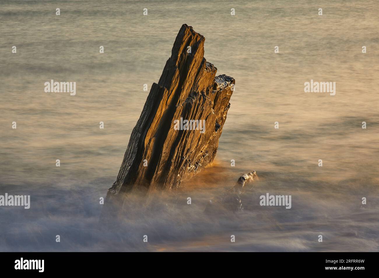 Küstenfelsen, die von Wellen bei aufsteigender Flut bei Sonnenuntergang gewaschen werden; Ayrmer Cove, bei Kingsbridge, an der Südküste von Devon, Großbritannien. Stockfoto
