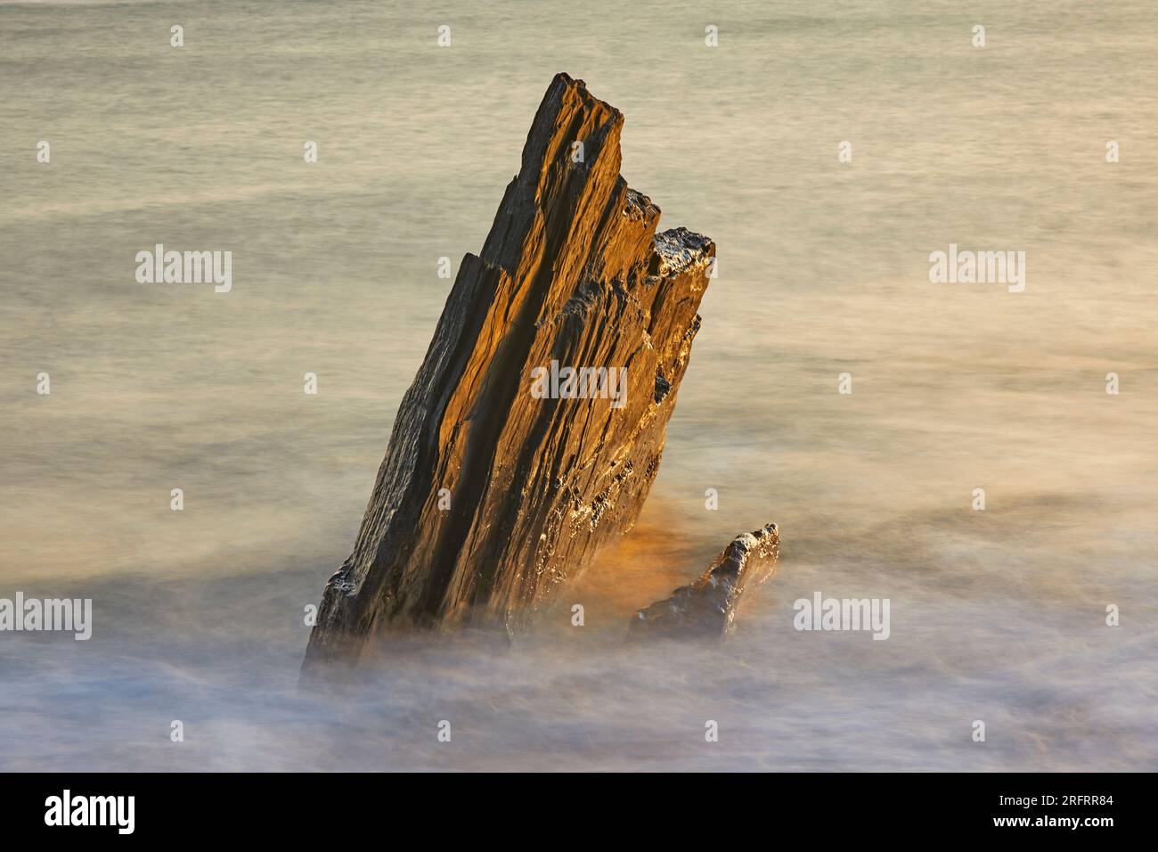 Küstenfelsen, die von Wellen bei aufsteigender Flut bei Sonnenuntergang gewaschen werden; Ayrmer Cove, bei Kingsbridge, an der Südküste von Devon, Großbritannien. Stockfoto