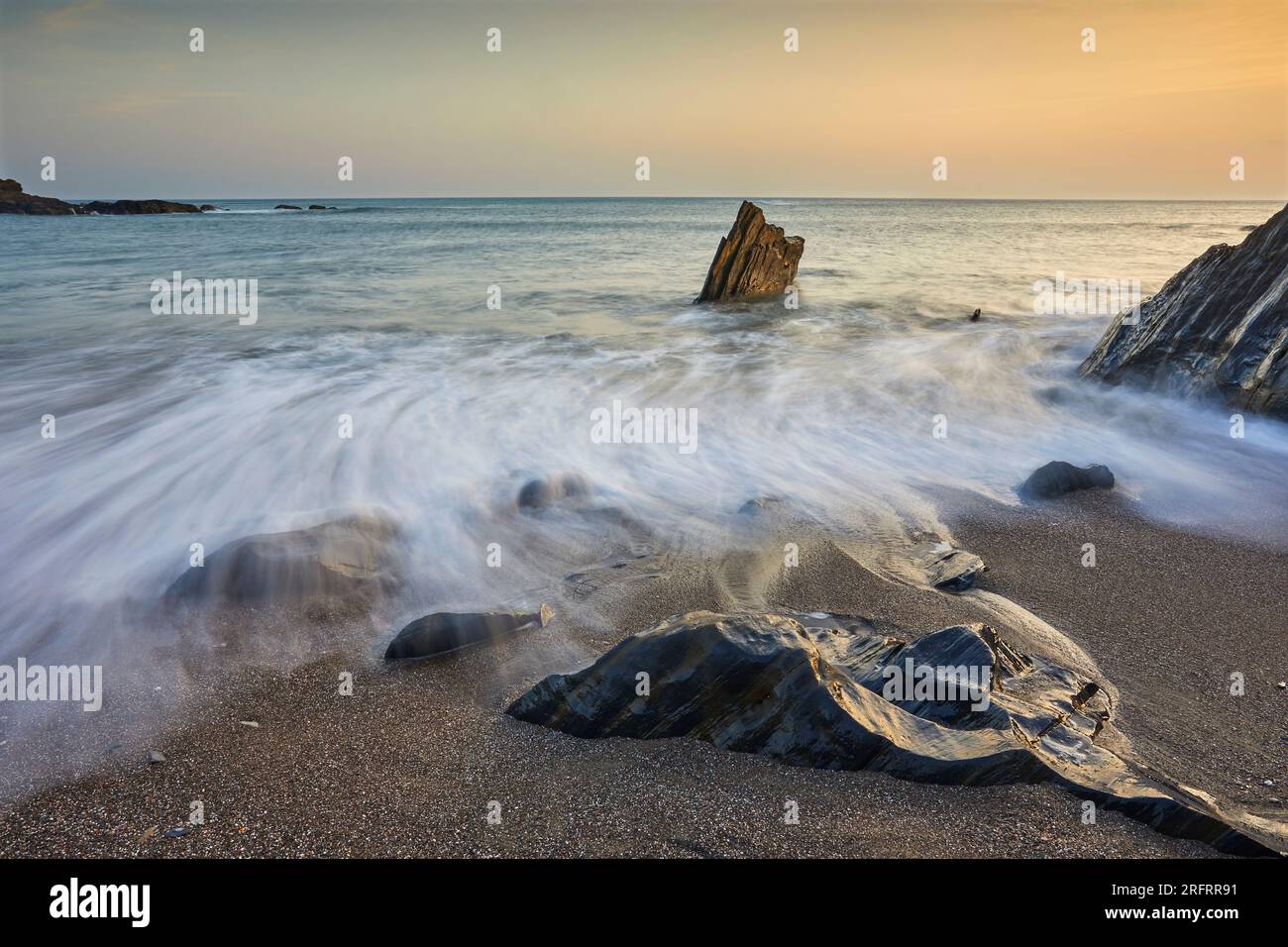 Küstenfelsen, die bei Sonnenuntergang von Wellen bei aufsteigender Flut gewaschen werden; Ayrmer Cove, bei Kingsbridge, an der Südküste von Devon, Großbritannien. Stockfoto