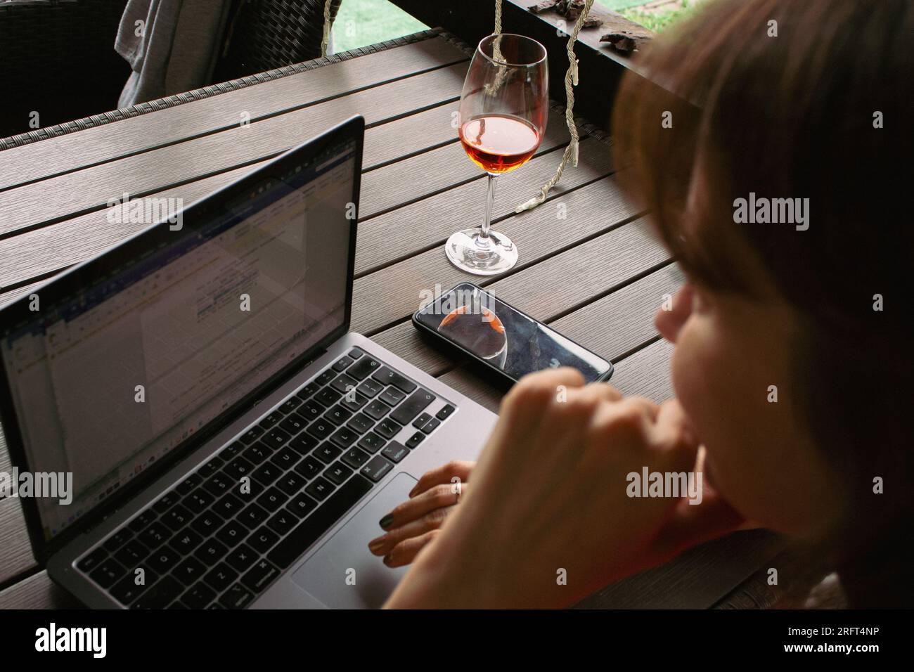 Ein Mädchen tippt auf einem Laptop mit Weinglas. Frau, die an einem kabellosen Computer in einem Café im Freien arbeitet. Freiberufler in der Öffentlichkeit. Moderner Lifestyle. Stockfoto