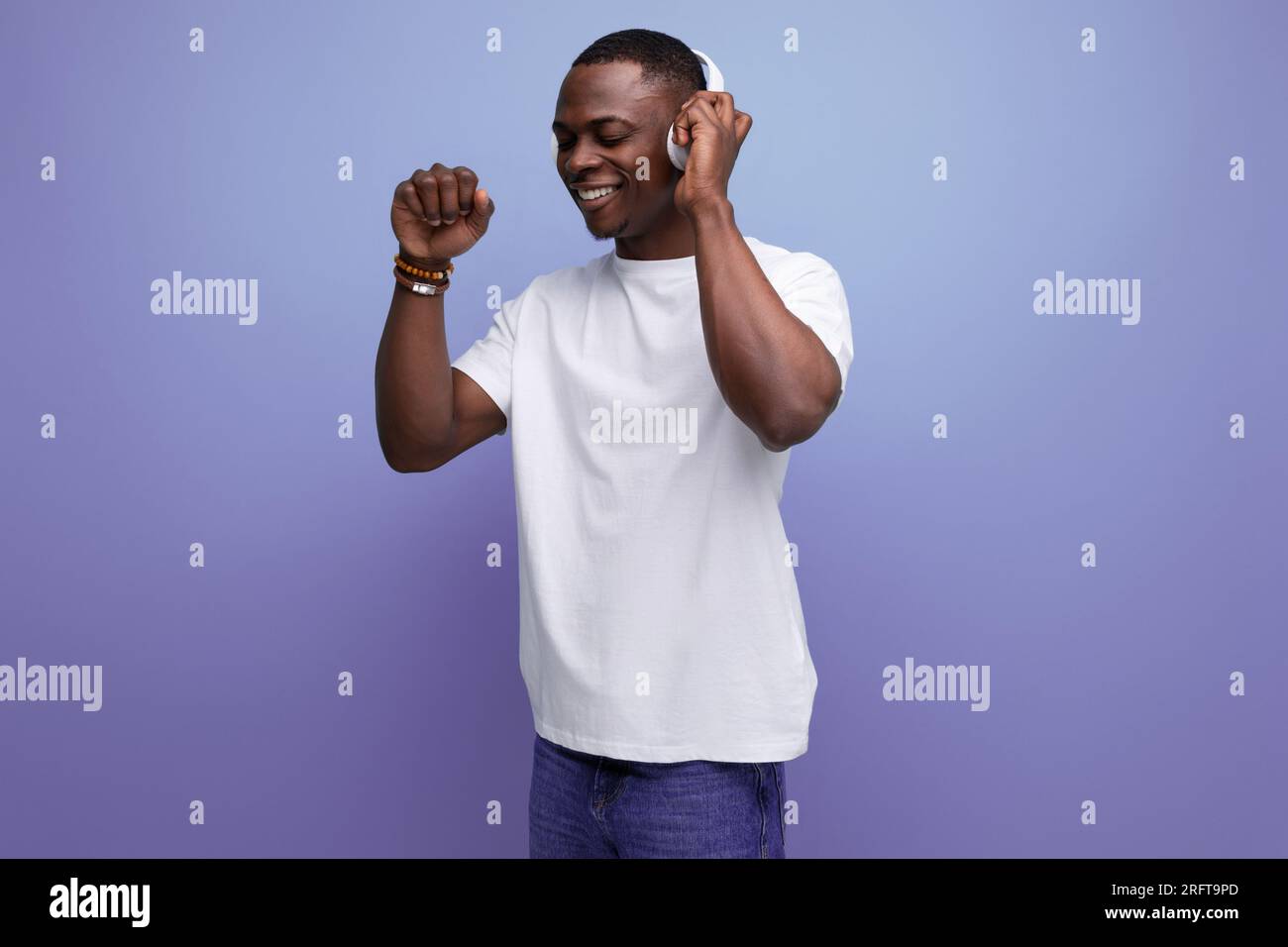 Ein energiegeladener junger, dunkelhäutiger amerikaner in einem weißen T-Shirt hört sich einen Podcast mit Kopfhörern an Stockfoto