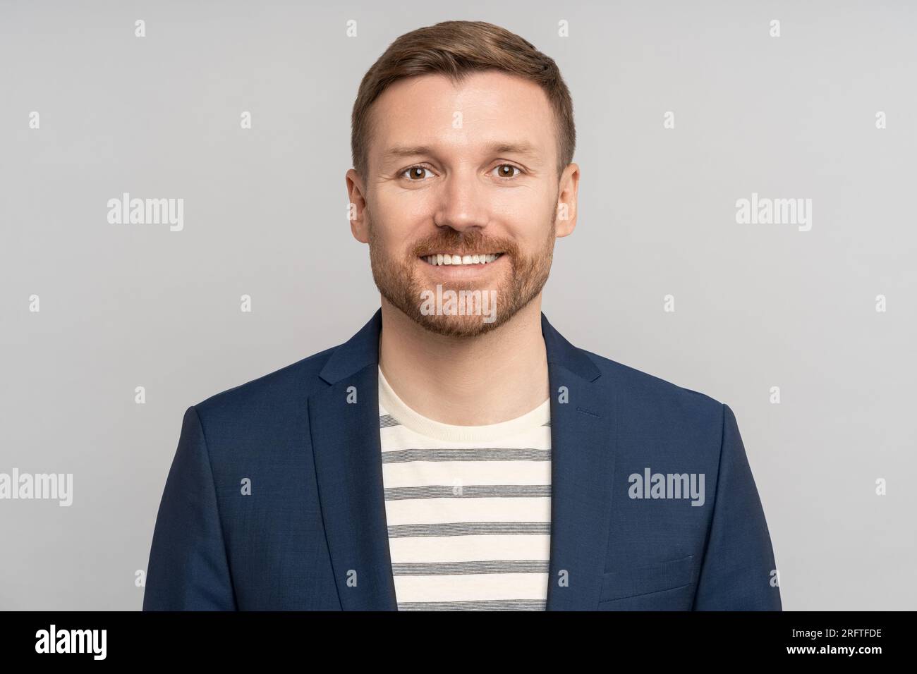 Ein selbstbewusster Unternehmer mit positiven Emotionen lächelt auf einem grauen Studiohintergrund Stockfoto