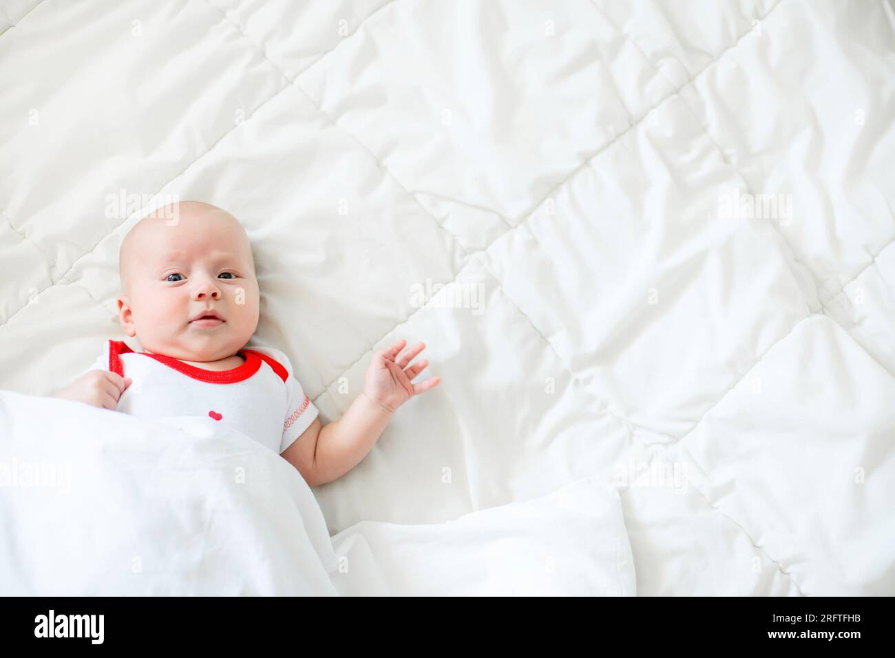 Babypflege, die Gefahr, mit den Eltern im Bett zu schlafen. Baby unter schwerer weißer Decke Stockfoto