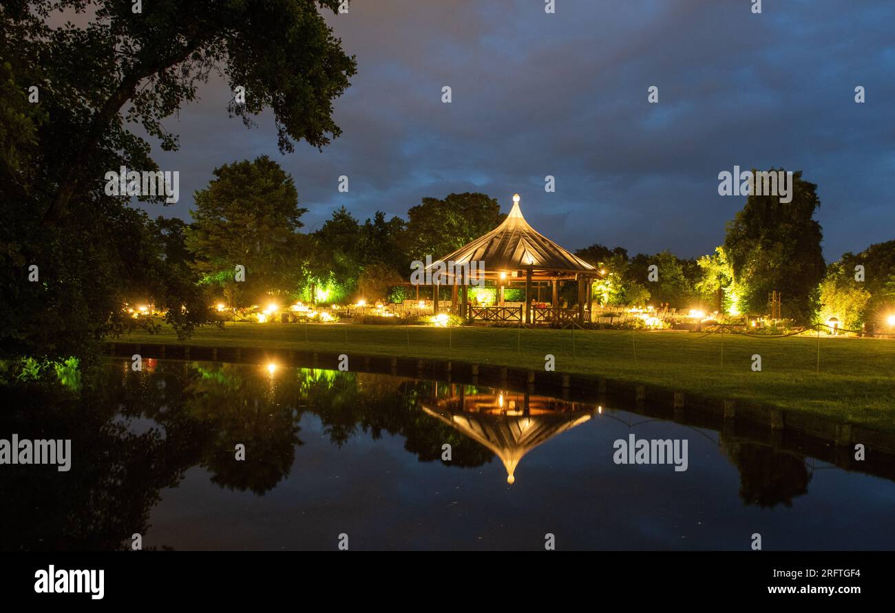 Augsburg, Deutschland. 05. Aug. 2023. Während der Lichterzauber stehen die Lichter im Botanischen Garten neben dem beleuchteten Rosenpavillon, der sich in einem Teich spiegelt. Jeden Samstag, bis zum 13. August, gehen im Botanischen Garten unzählige Lichter in der Dämmerung an. Zu diesem Zweck ist der Botanische Garten bis Mitternacht geöffnet. Kredit: Stefan Puchner/dpa/Alamy Live News Stockfoto