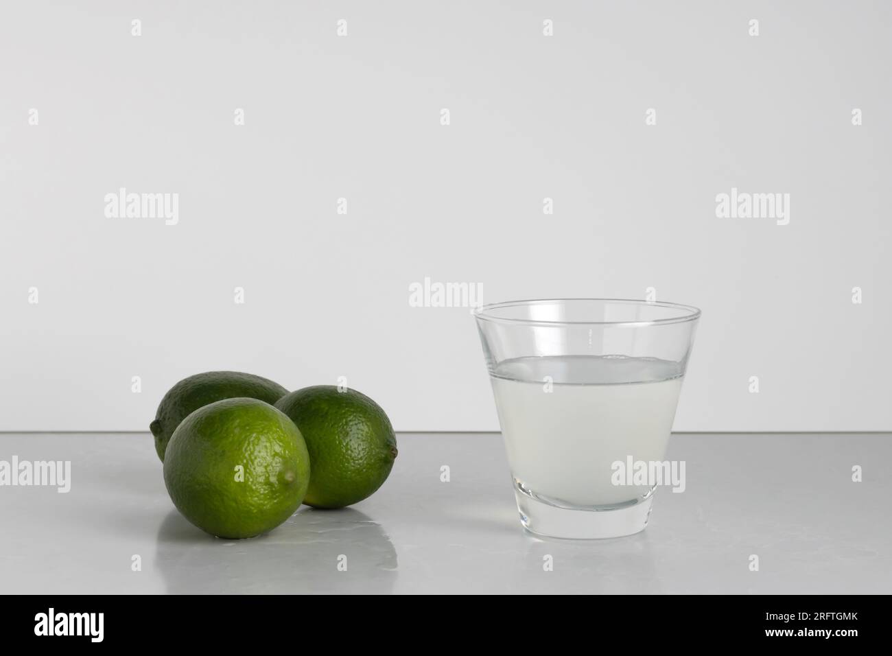 Glas Limettenwasser mit einer Gruppe von drei ganzen Limetten auf weißem Hintergrund mit Kopierraum Stockfoto