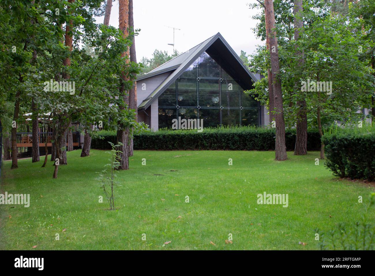 Blick auf ein Restaurant im Wald. Wunderschönes Gebäude mit Panoramafenstern. Vor den Fenstern - Kiefern und Rasen. Der Schaden am Gebäude Stockfoto