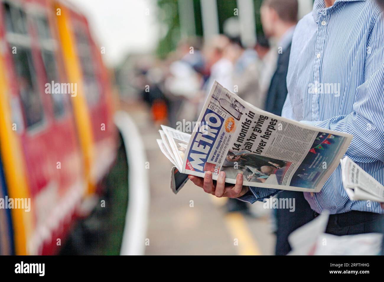 Nahaufnahme eines Pendlers, der die Metro-Zeitung auf dem Bahnsteig liest und auf den Zug in Norbition Station, Surrey, England wartet. Stockfoto