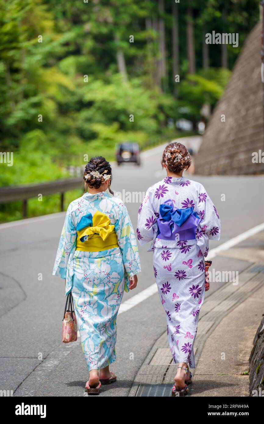 Rückansicht von zwei Frauen mit japanischem Yukata-Sommerkimono, die auf der Straße in der Natur von Kyoto, Japan, spazieren. Stockfoto