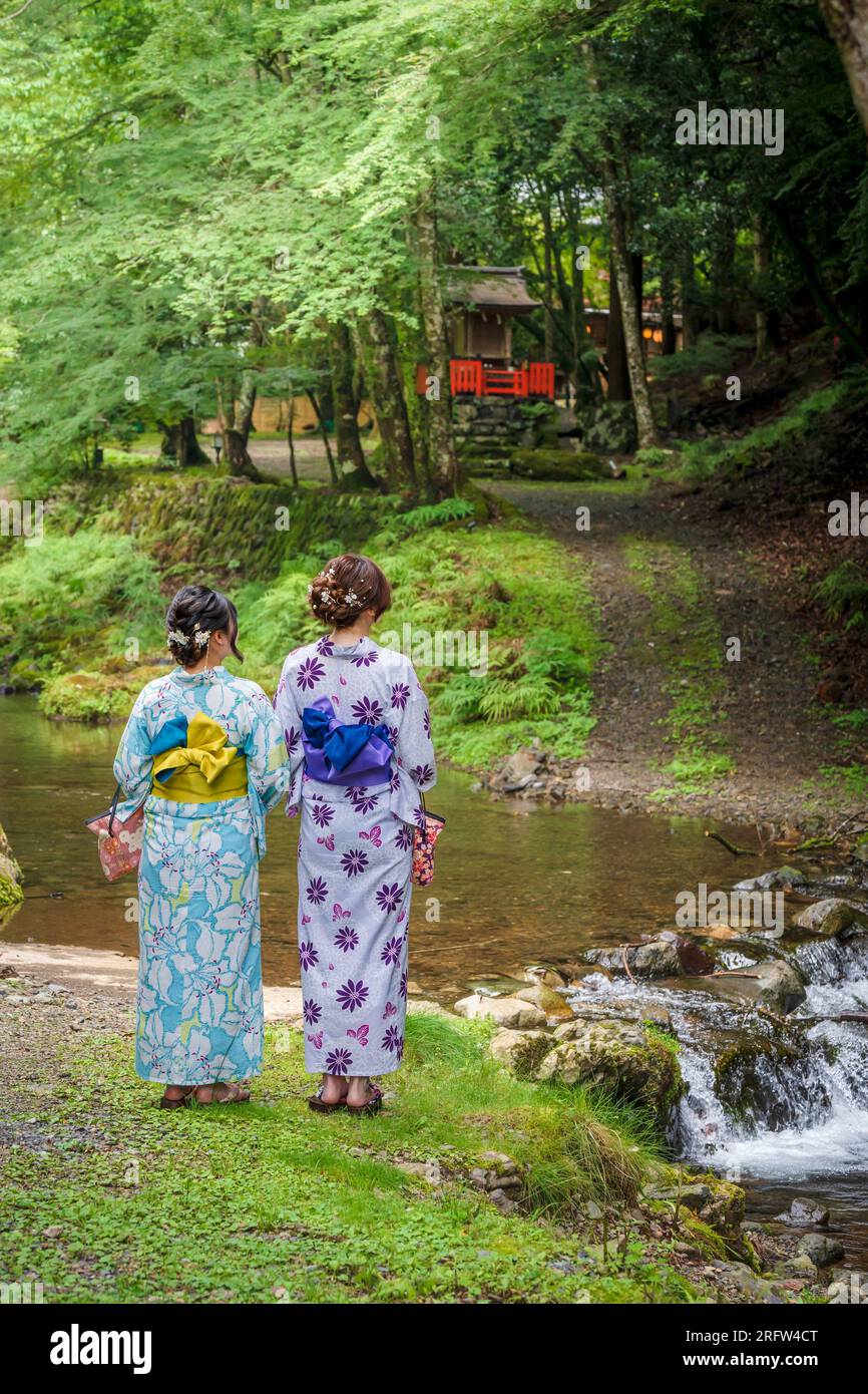 Rückansicht von zwei Frauen mit japanischem Yukata-Sommerkimono, die neben einem Fluss im Naturwald stehen. Kyoto, Japan. Stockfoto